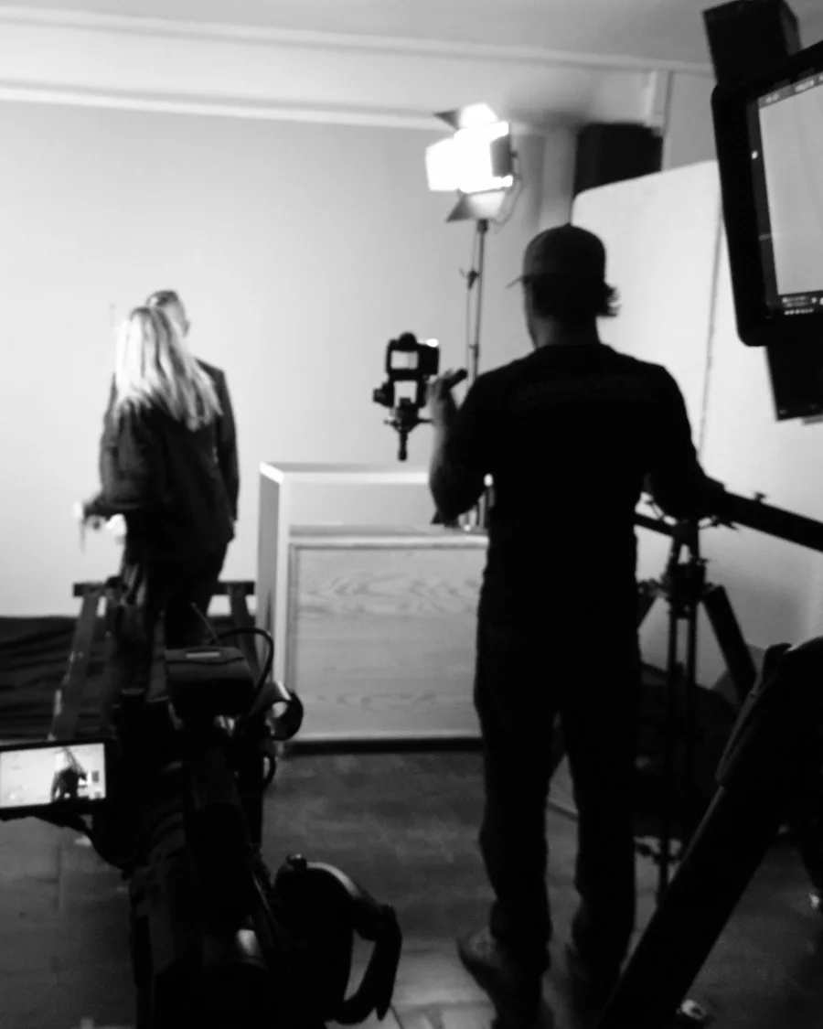 Dreh im Studio: Kameramann mit Gimbal, davor die Darstellerin vor grauer Wand, im Bild Licht und Monitor